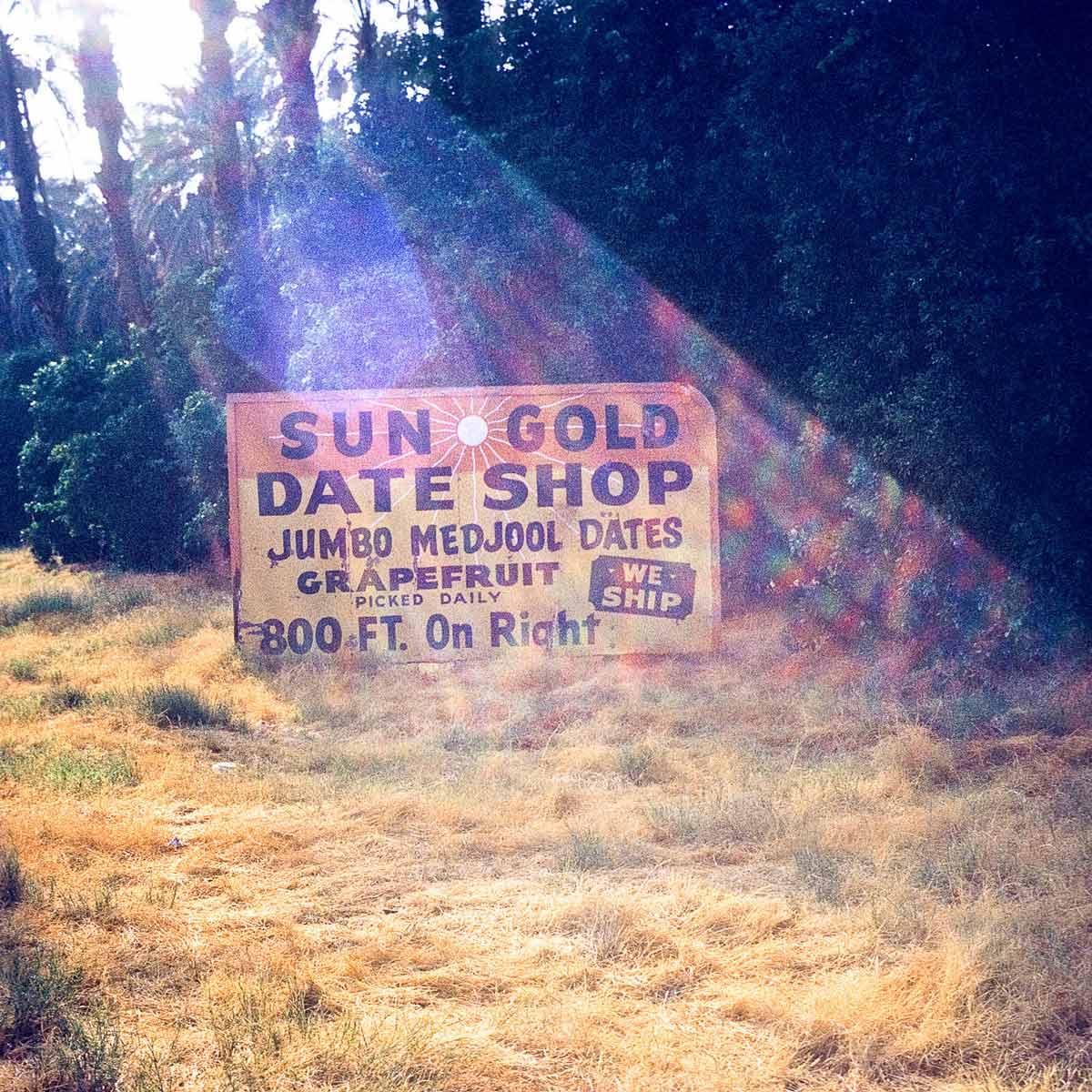 A sign in a sunny clearing that says "Sun Gold Date Shop" 