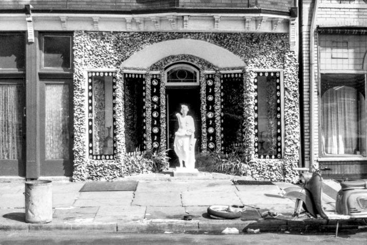 A white figurative statue in front of a heavily textured storefront in Passaic, New Jersey