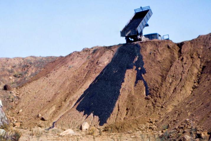 a truck dumping black asphalt onto an earthen hillside