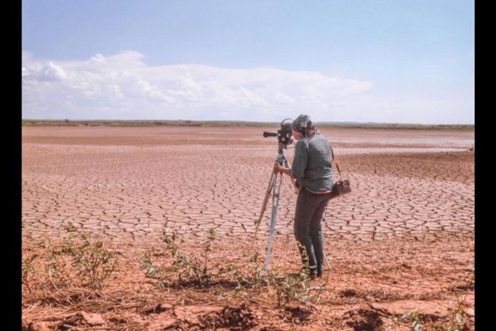 A person looking through a film camera on a tripod, overlooking a dry lakebed.
