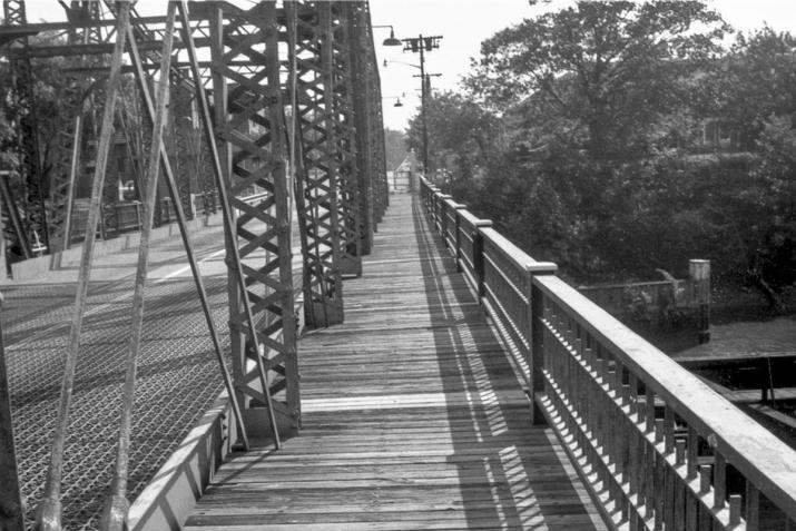 looking down a bridge with a wooden walkway in the center. black and white.
