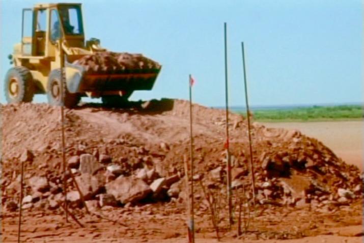 a yellow front loader on top of a ramp of red earth