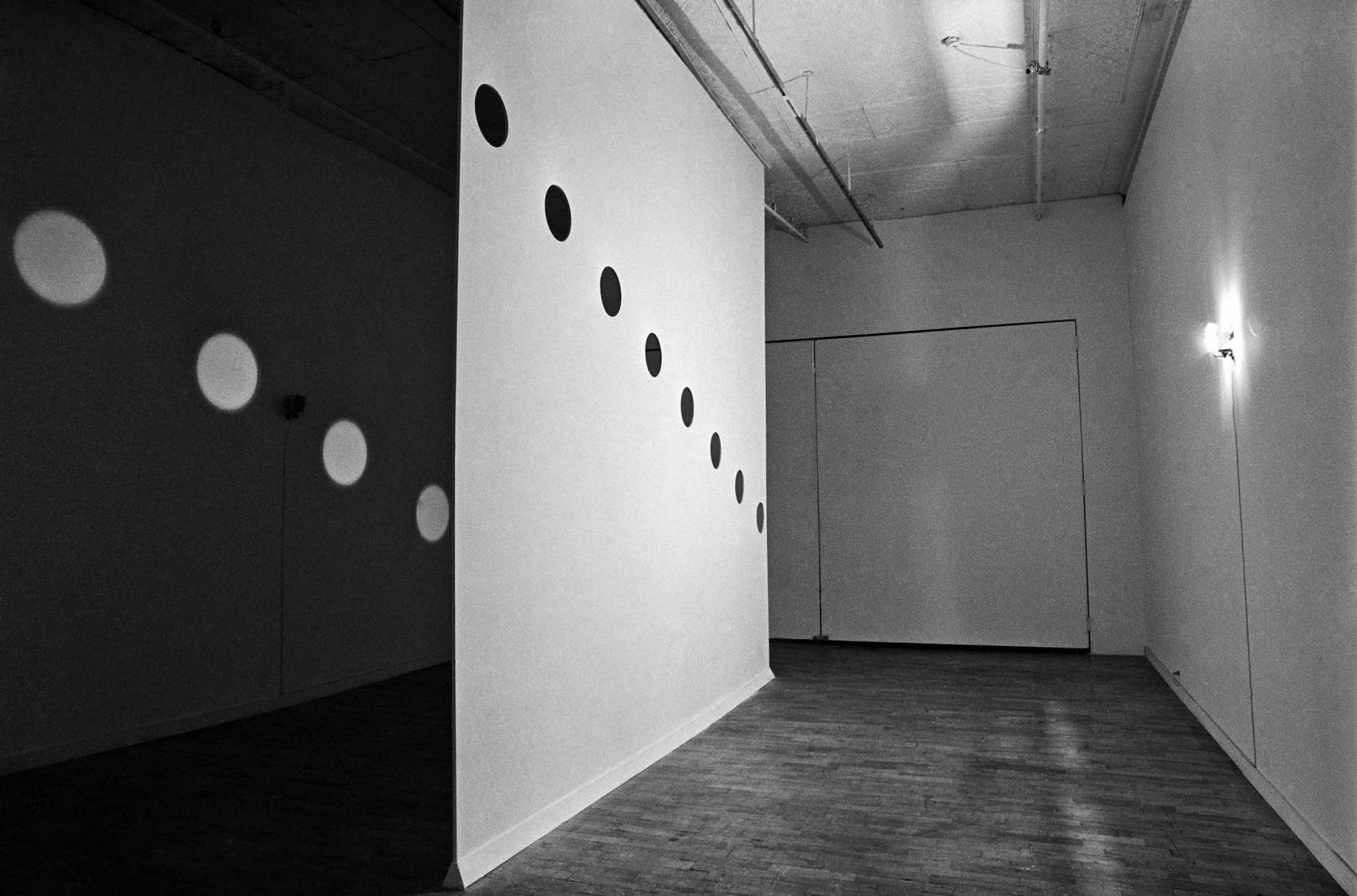 Room bisected by a wall with circular holes cut in it to let light pass through, creating orbs of light on the other side.