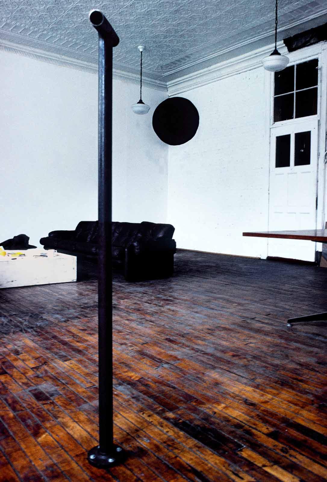 Stell pipe in a room with wood floors, white walls, and a black circle painted in the corner of the room.