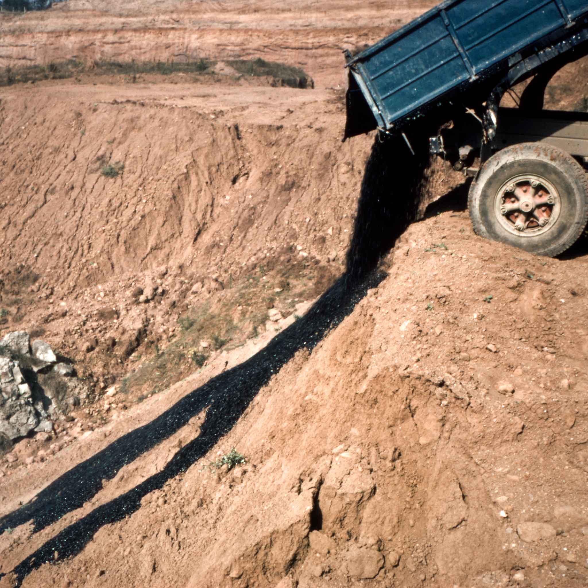 A dump truck unloads a large amount of asphalt which runs down the side of a hill outside of Rome, Italy.