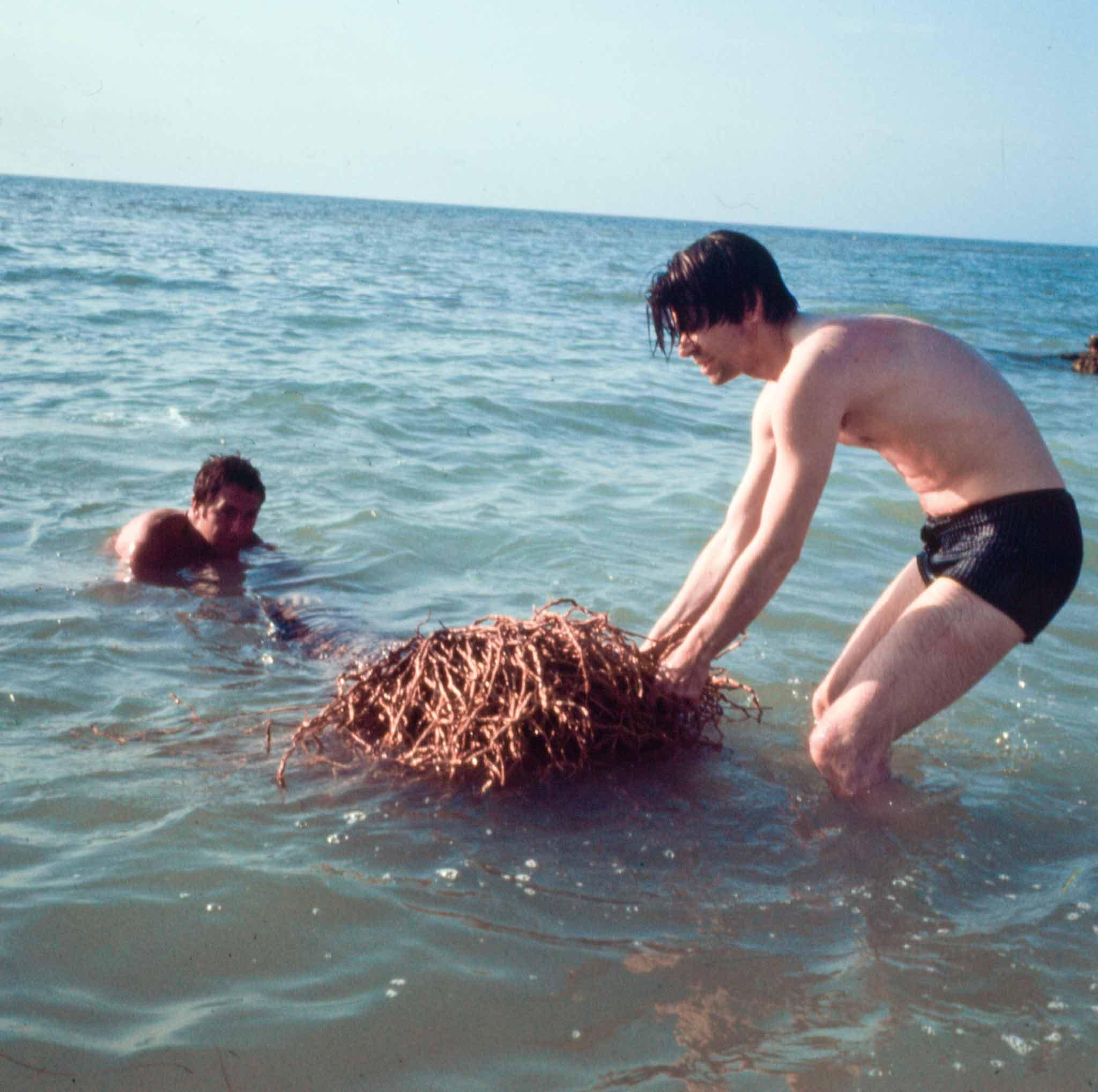 Robert Smithson with Robert Rauschenberg taking a floating, waterlogged tree out of the ocean off Captiva Island in Florida. This tree, which includes the root system, will become Smithson's first Upside Down Tree work.. 