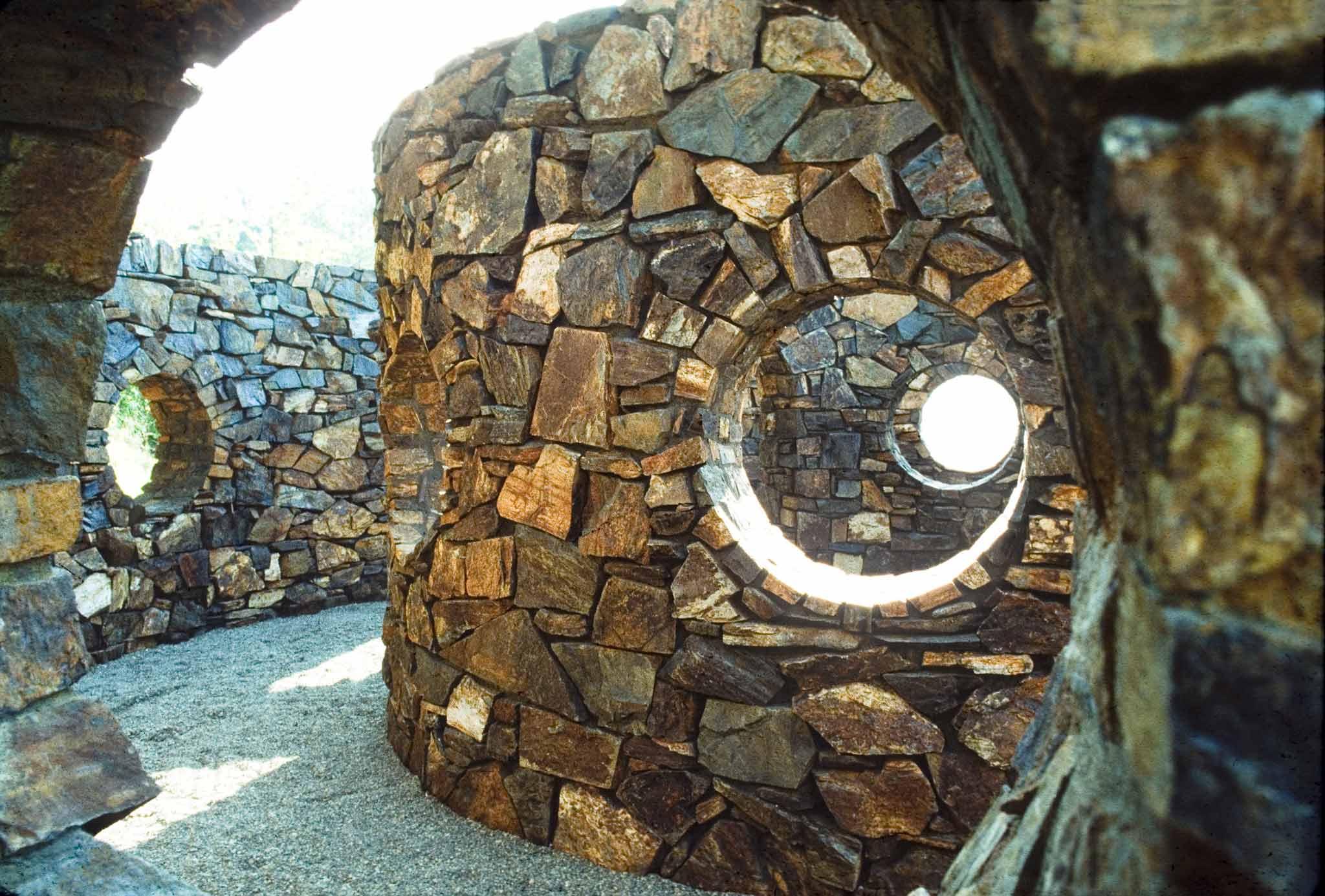 Looking through a circular opening at another curved stone wall with another circular opening in it.