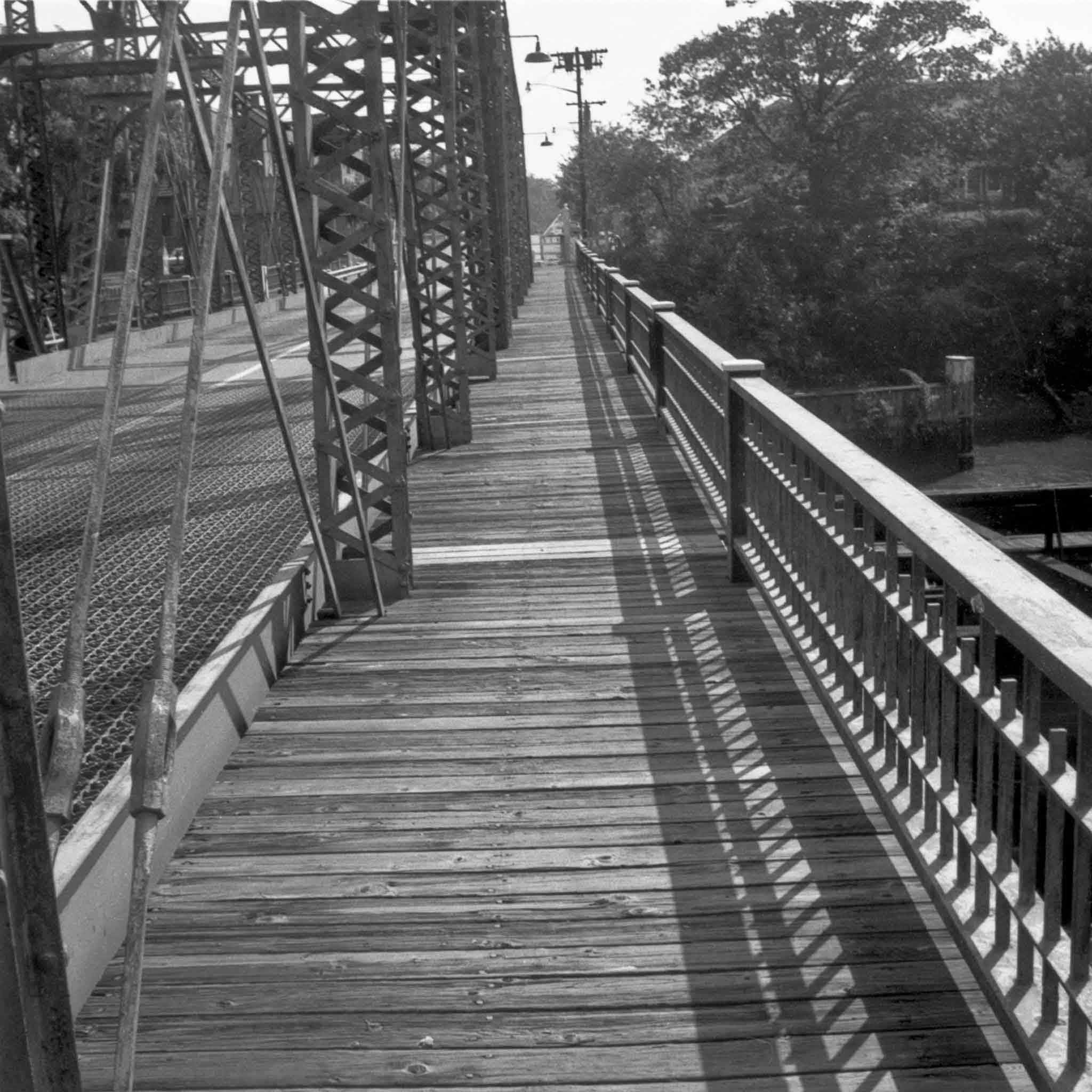 black and white image of a wooden walkway on a metal truss bridge with trees in the background