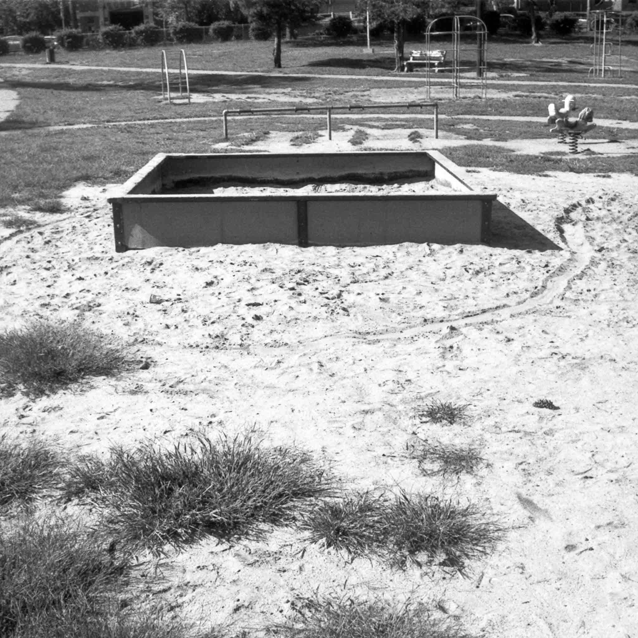 black and white image of a sandbox with a playground in the backgroud