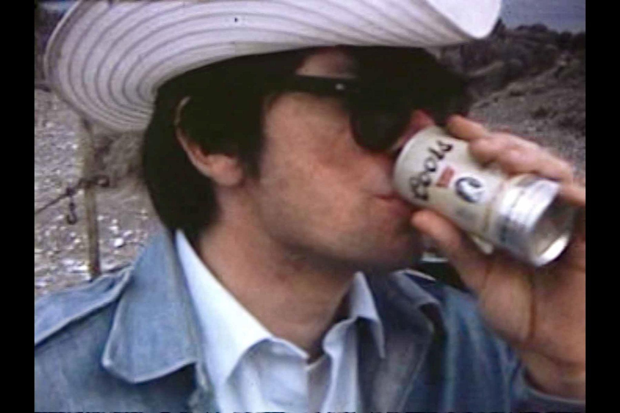 A man wearing a cowboy hat drinking a Coors beer