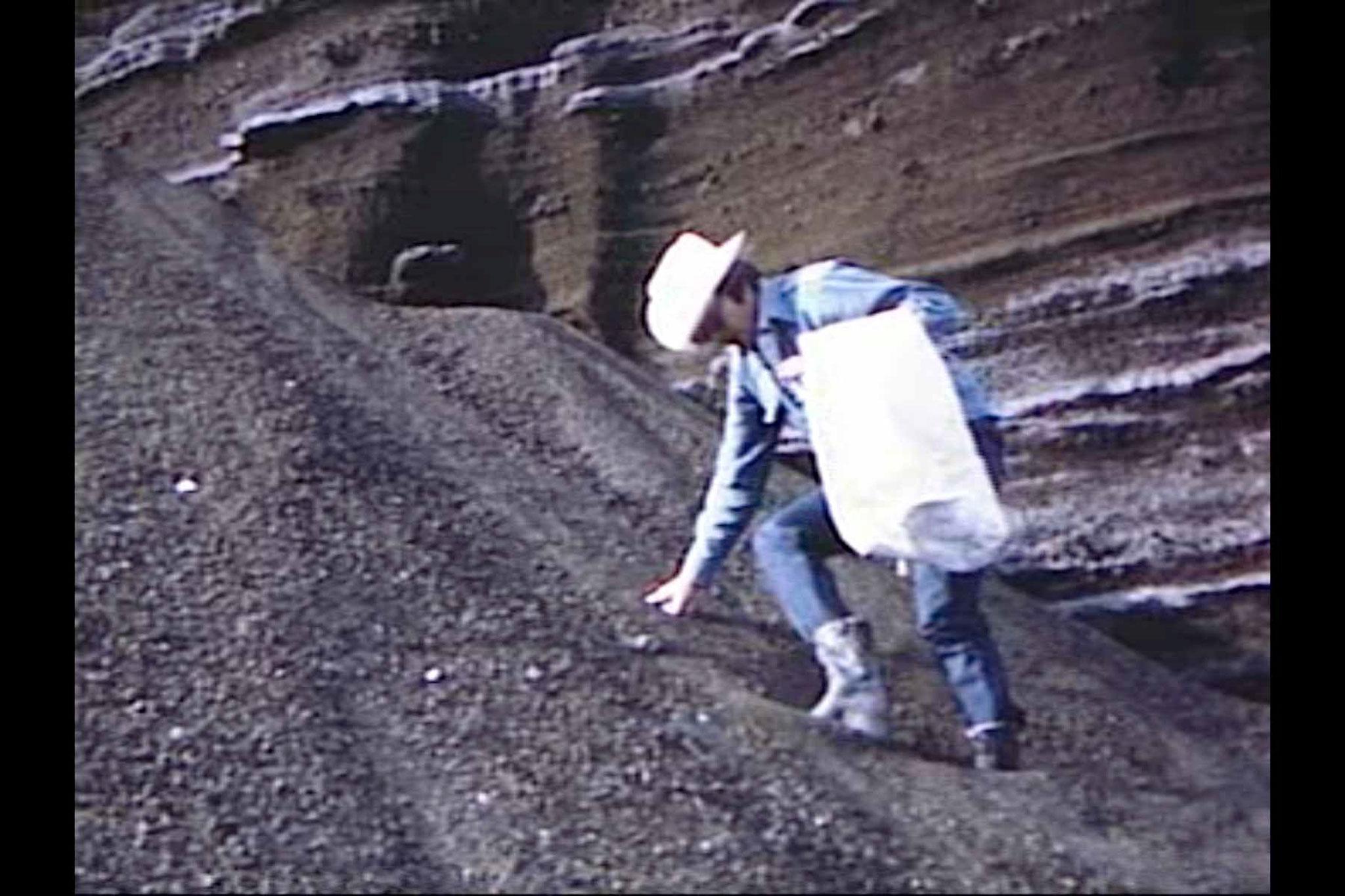 A man wearing a cowboy hat descending a steep slope of gravel