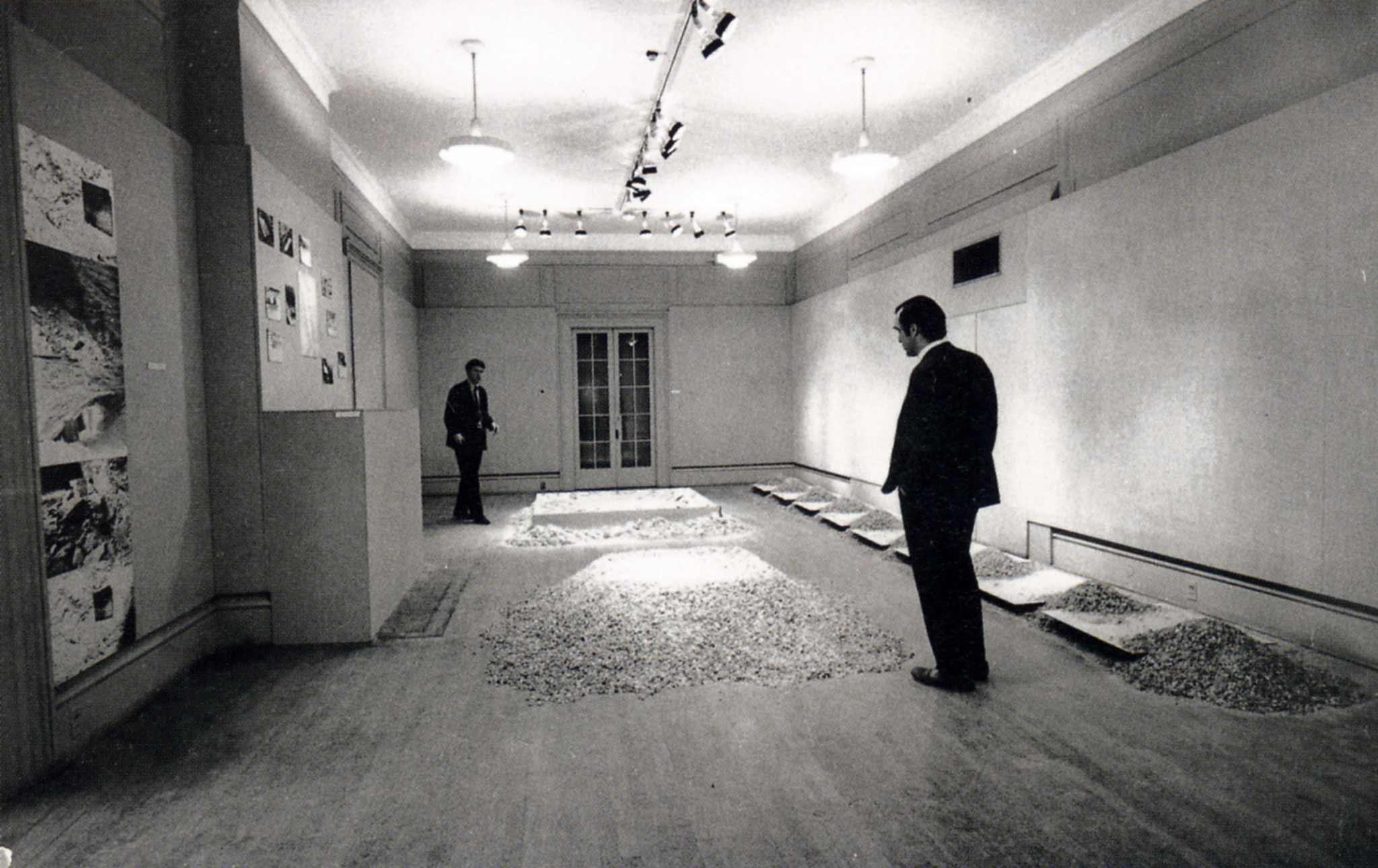 two figures in a room filled with sculptures made of salt and mirrors on the floor and photographs on the wall, black and white