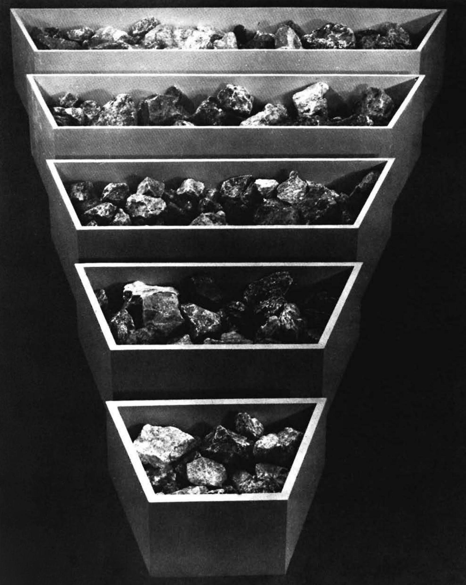 five polygon shaped bins arranged from largest at the top to smallest at the bottom filled with rocks