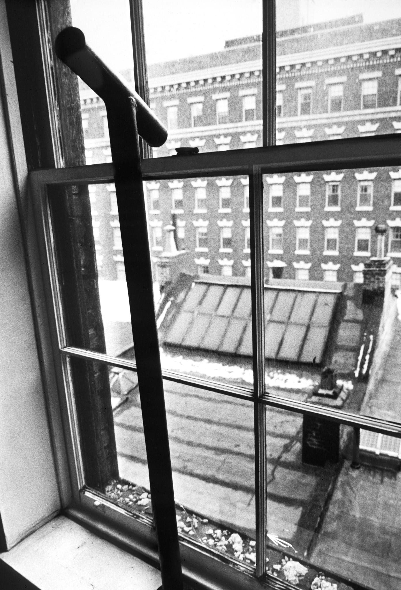 a metal pipe with a short angled pipe welded to the top pointing out a window in New York city looking down on a building