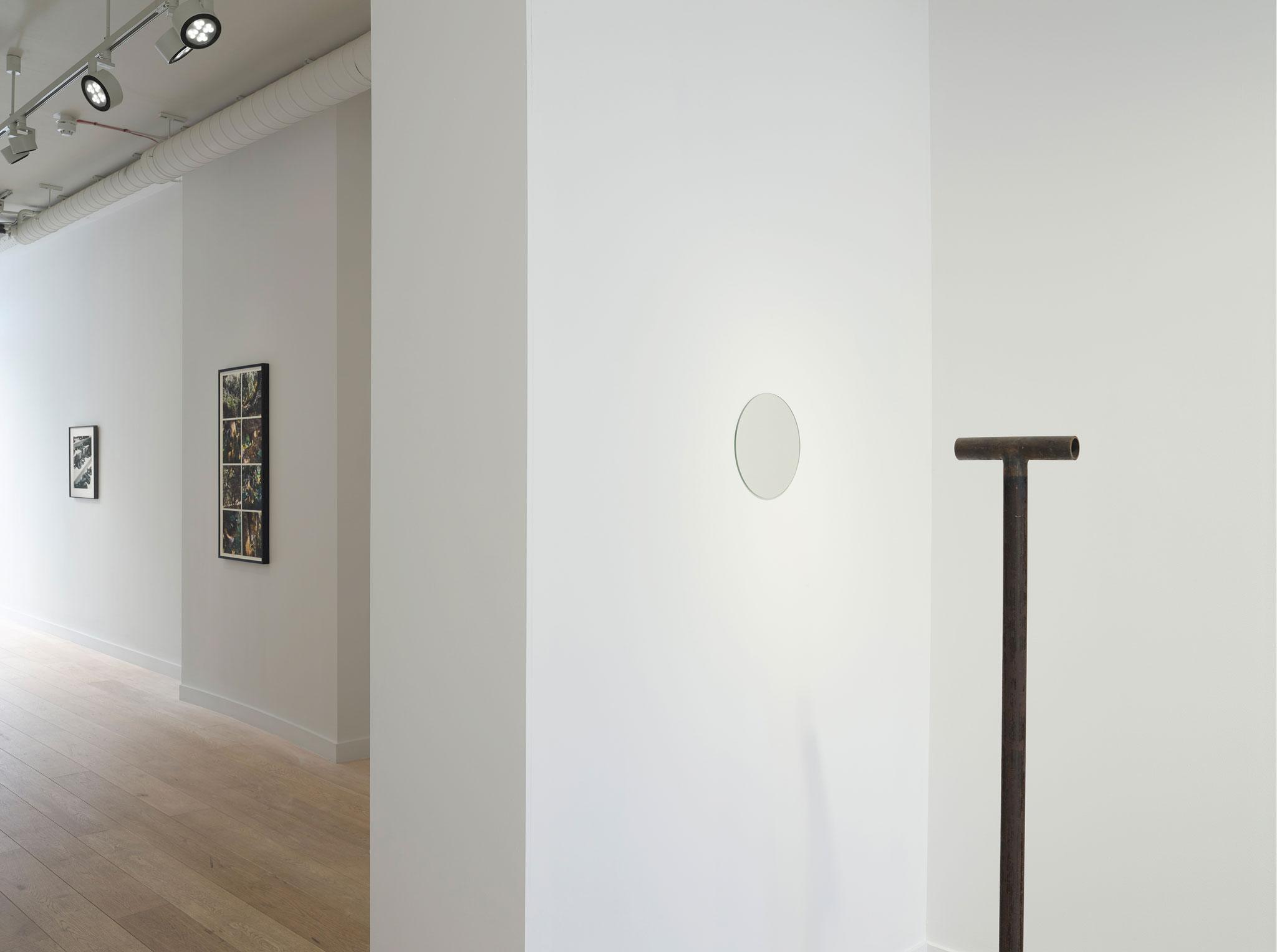 an art gallery with a sculpture made of metal pipe that points at a circular mirror on a wall