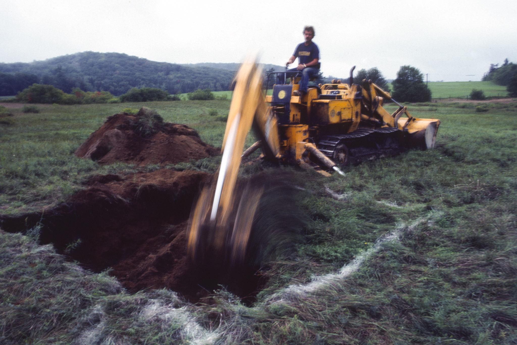 a large digging machine digs a square hole in a green grassy field