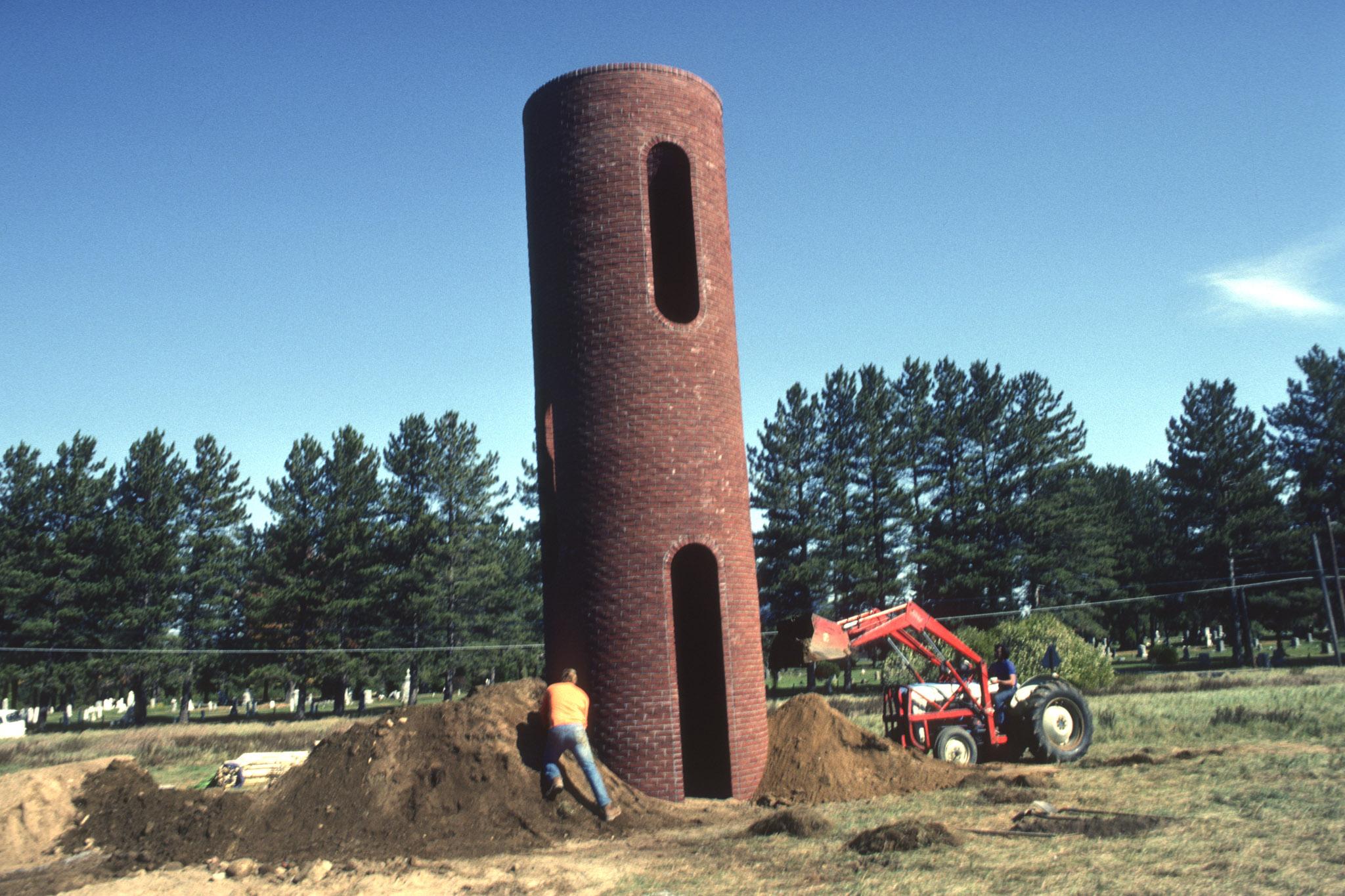 construction of a large cylindrical tower made using brick and two workers piling dirt around the base