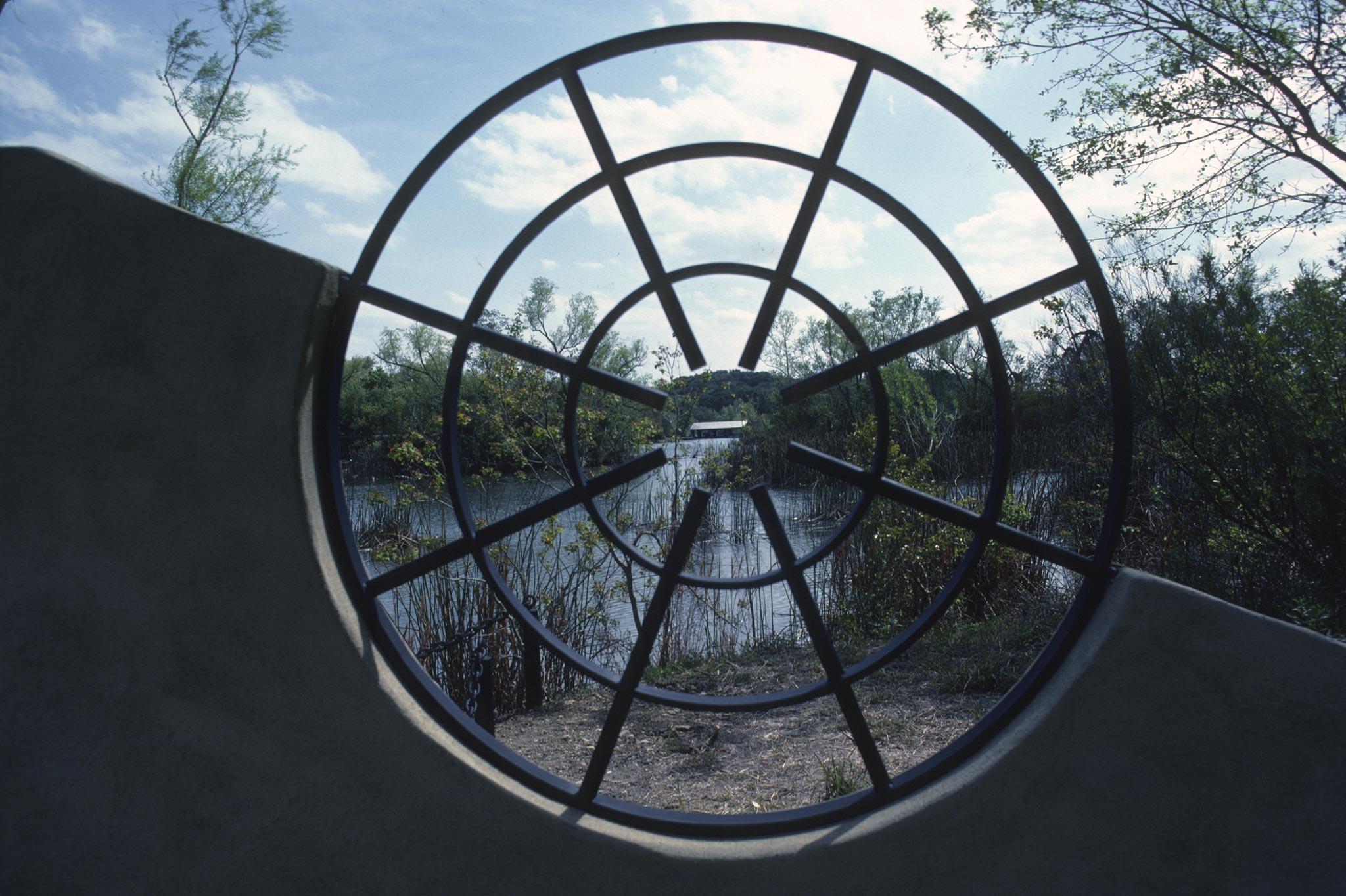 a circular metal grate frames a building across a body of water
