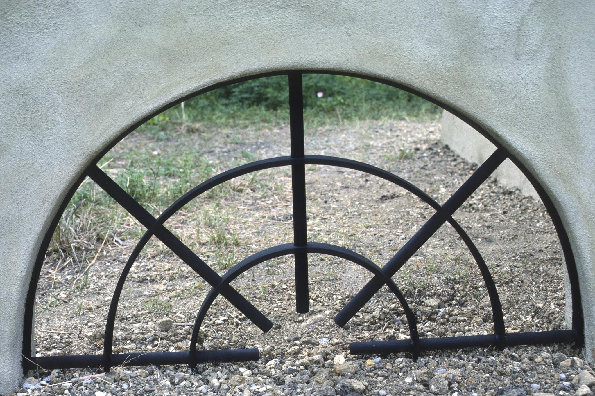 a metal grate in the shape of a half circle that is built into a small stucco wall, right above gravel