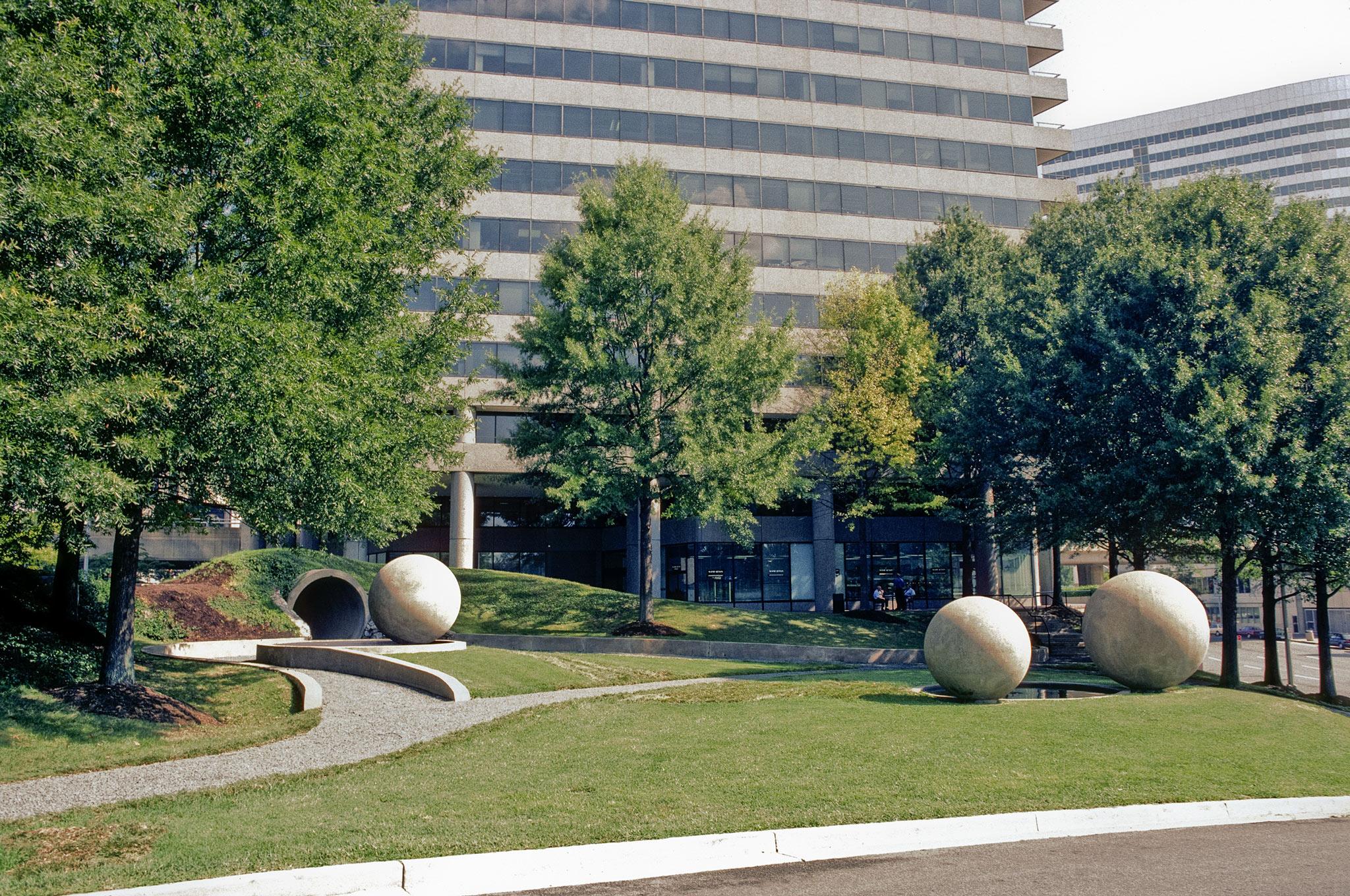 three large concrete spheres in a grassy park surrounded by trees and tall buildings