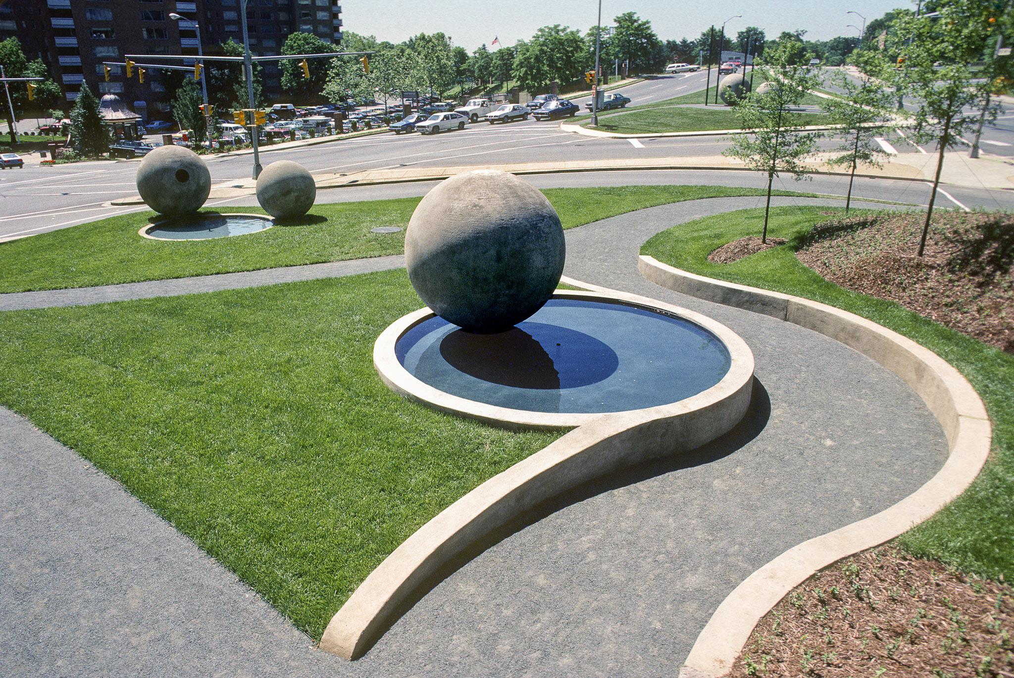 large concrete spheres in a park. One of the spheres rests above a circular pool and a meandering path