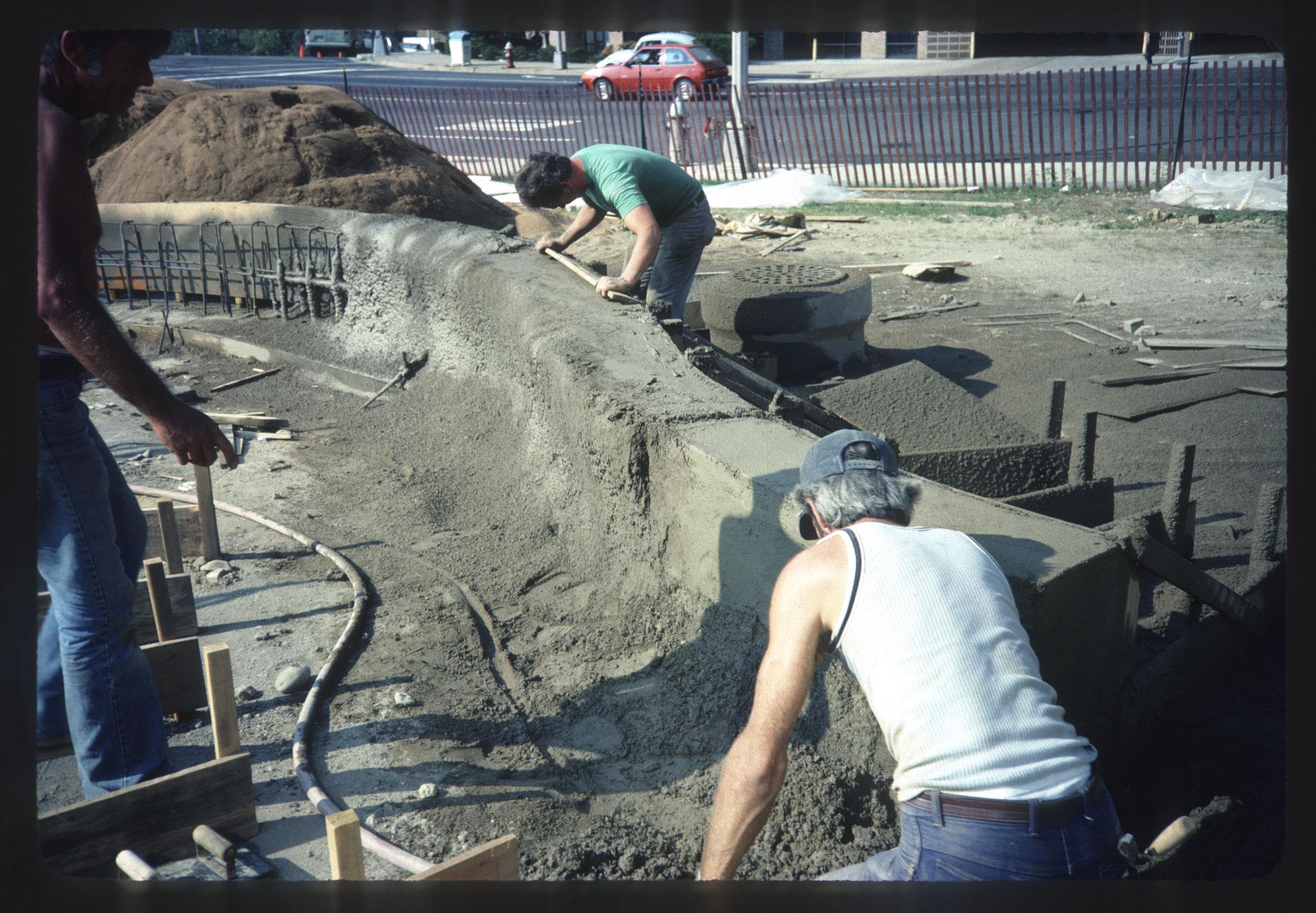 three people working on a low concrete wall