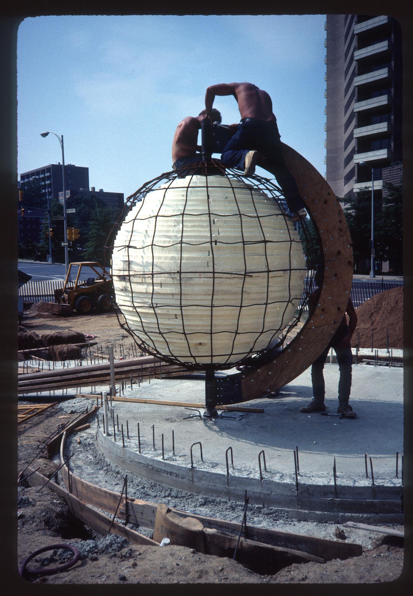 three people working on the armature for a large concrete sphere