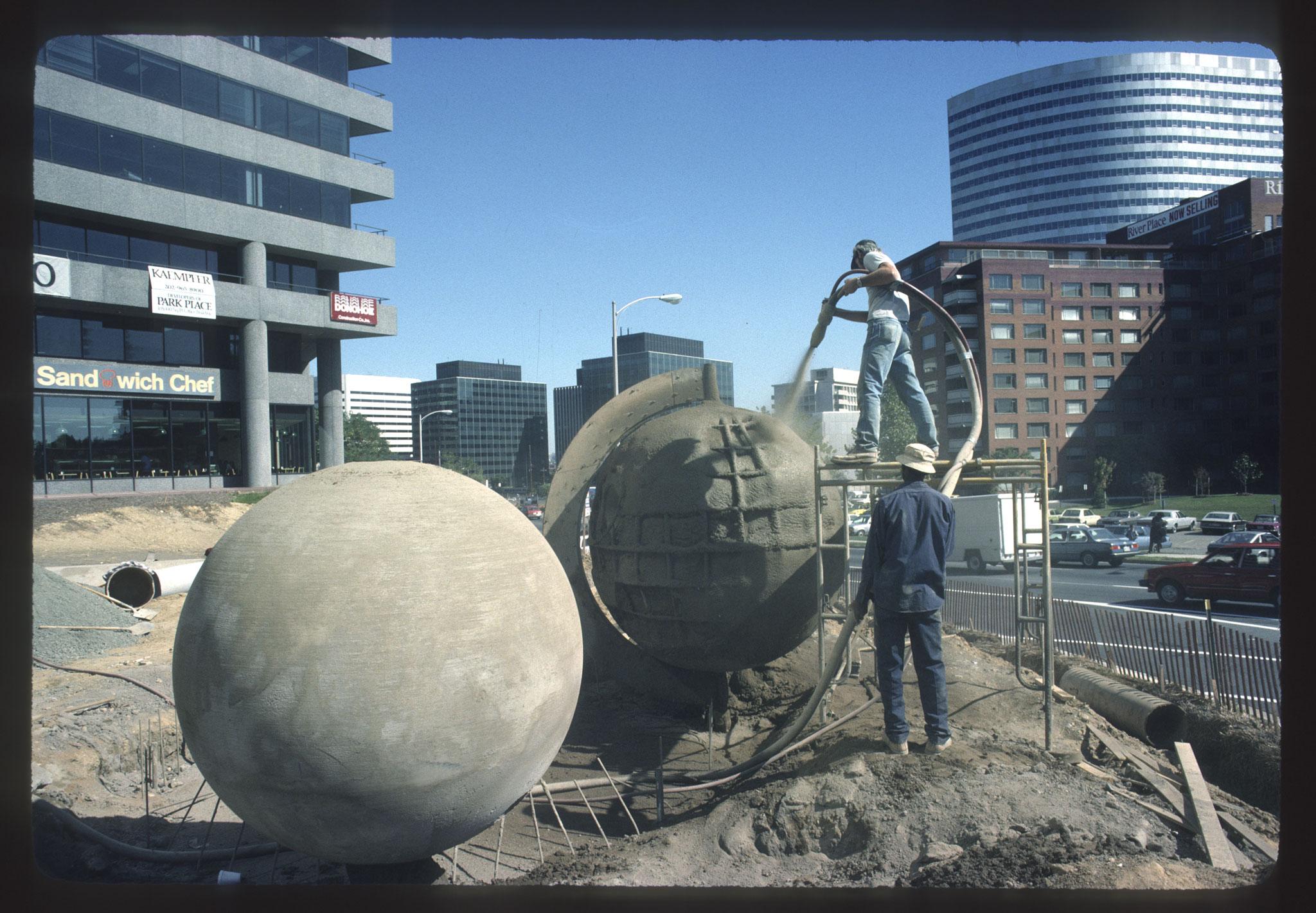 two people shooting concrete onto a large sphere in an urban setting