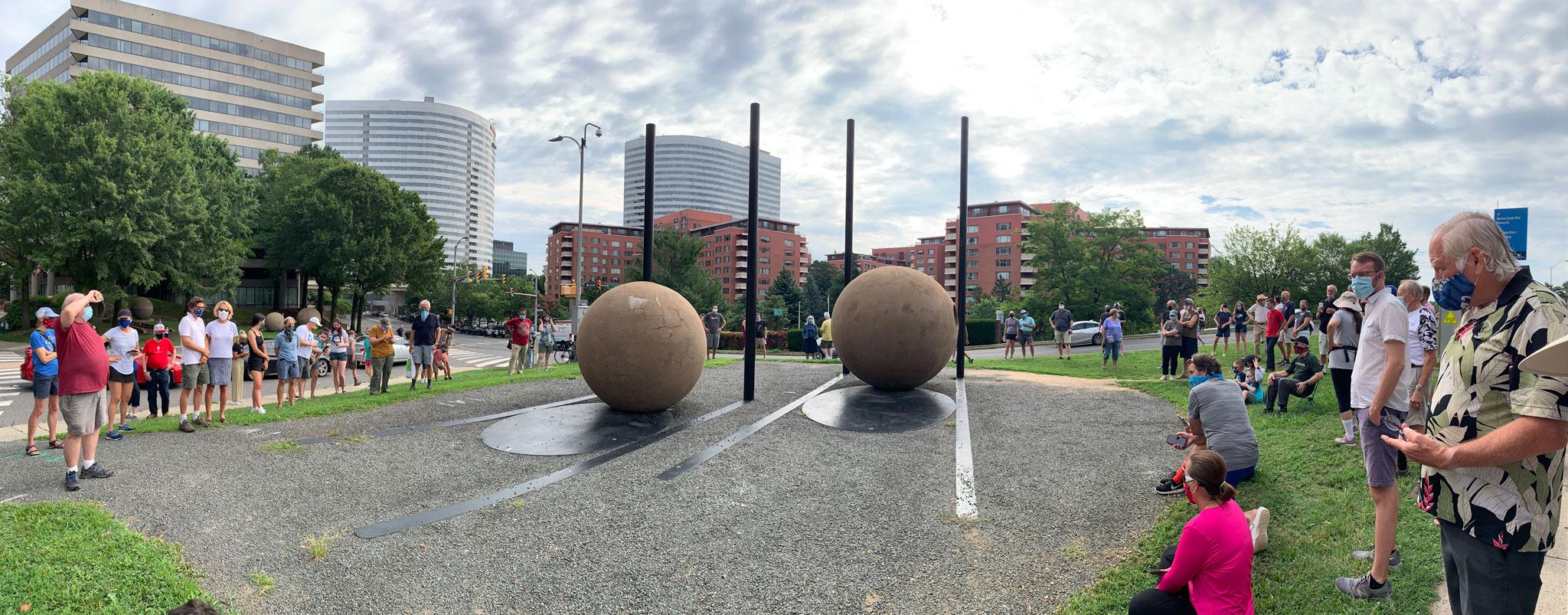 A group of people gathered around large spheres and poles for the shadow alignment of Nancy Holt's Dark Star Park