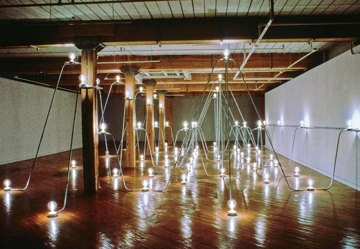 A series of interconnected steel conduit and lightbulbs in a room. 