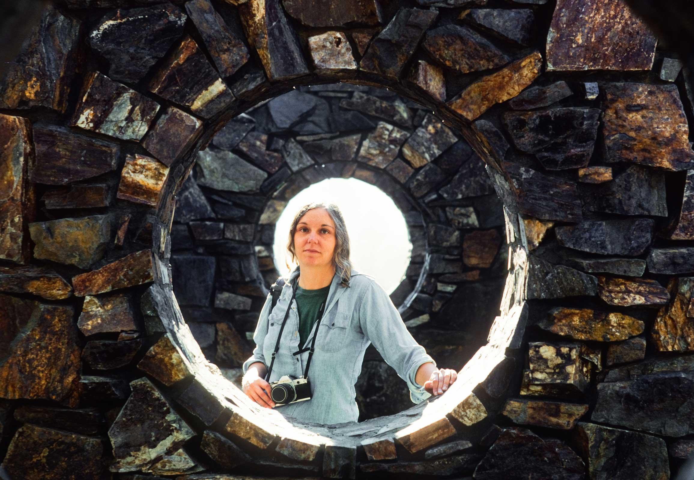 Nancy Holt standing in a circular hole at her work Stone Enclosure: Rock Rings