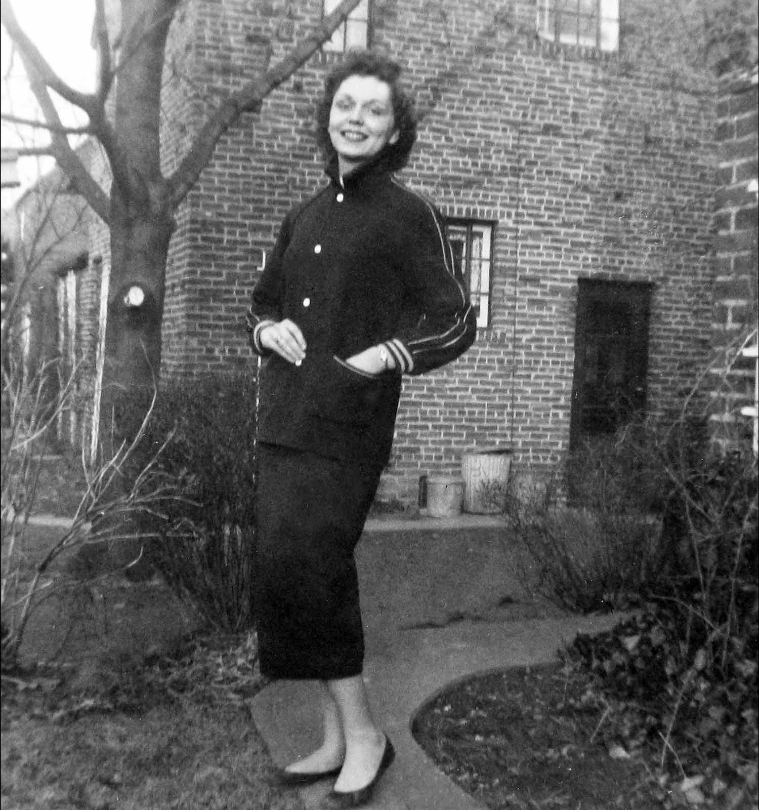 Black and white image of Nancy Holt standing outside a brick building